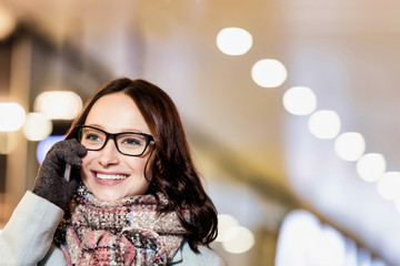 Portrait of young attractive woman talking on smartphone at night shopping