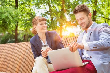 Wall Mural - Businessman discussing plans over laptop with beautiful businesswoman while sitting on bench