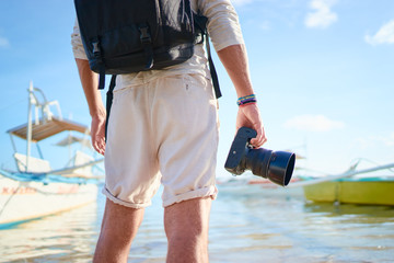 Photography and travel. Close up of young man holding camera enjoying beautiful sea view on fishing beach.