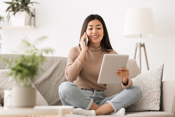 Cheerful girl making order by phone using digital tablet