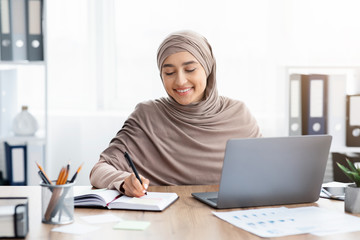 Wall Mural - Islamic businesswoman working on laptop in office and writing notes