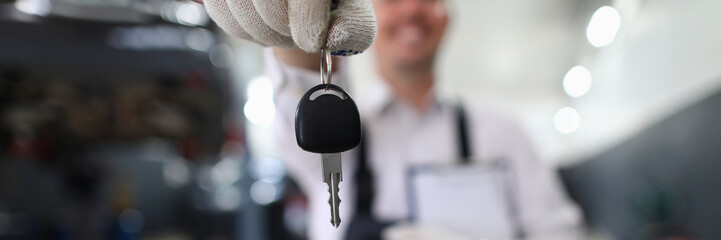 Focus on automechanic male hand holding automobile bunch of keys and important paper folder with information about fixed auto. Machinery checkup concept. Blurred background