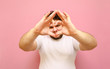 © bodnarphoto - Cheerful young overweight man showing heart gesture to camera over pink background and smiling. Funny fat man in a white T-shirt shows his heart with his fingers and looks into the camera.