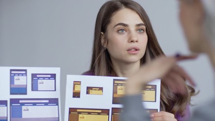 Wall Mural - Young female designer showing papers with application interface templates for different devices and discussing them with colleague