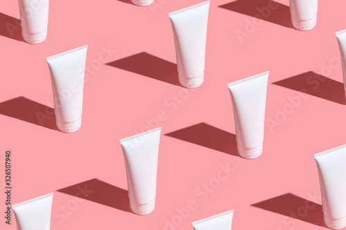 White cream tubes on light pink table. Care about face, hands, legs and body skin. Women beauty products. Cosmetic pattern. Empty place for logo on tubes. Hard light directly flat lay.