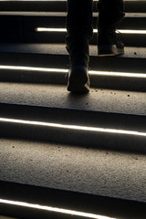 Female legs in suede boots climbing the lit stone steps on a winter evening. Bottom view.