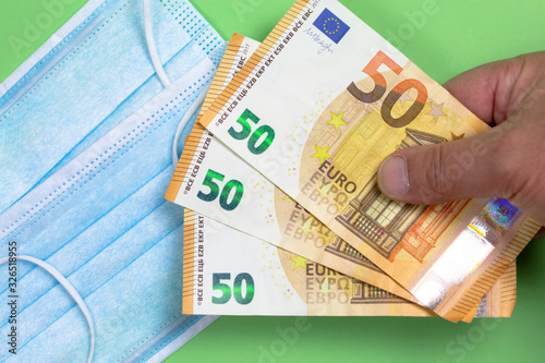 Fotomural Protective surgical mask with several 50 euro notes held by a man's hand to illu