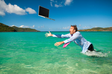 Helpless businessman leaping out of the water to save his laptop computer falling in bright blue tropical sea