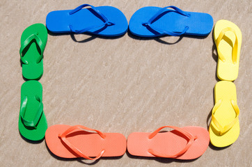 Wall Mural - Flip-flops in colorful orange, yellow, green, and blue forming a frame on textured sand beach
