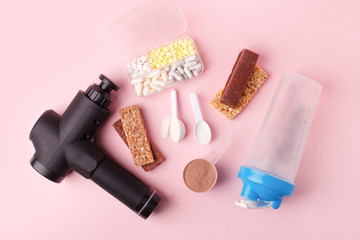 Wall Mural - Therapeutic percussive massage gun, fit meal, pills, sport energy bar on pink background - concept of modern sport activity and diet, health lifestyle routine, wellness, healthcare, copy space