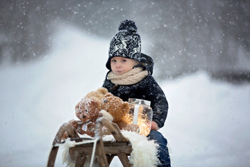 Poster - Cute boy playing with teddy bear in the snow, winter time. Little toddler playing with toys on snowy day