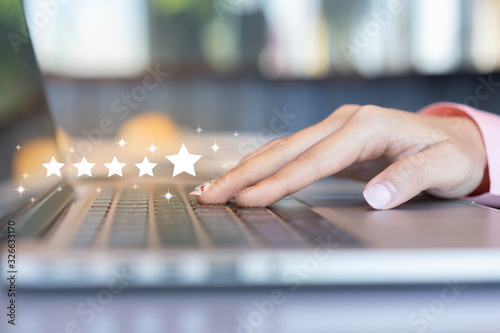 close up on customer woman hand pressing on laptop keyboard with  five star rating feedback icon and press level excellent rank for giving best score point to review the service , technology business