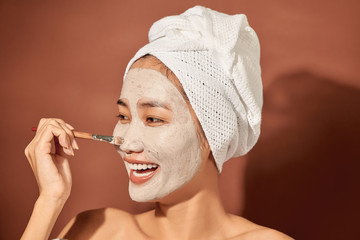 Wall Mural - Young beautiful woman with clay mask on her face. Salon skin care, natural cream of algae.