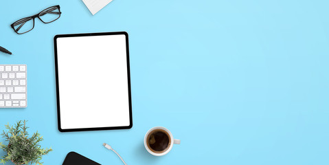 Tablet mockup on blue work desk with plenty of space for text. Top view, flat lay scene with up of coffee, keyboard, glasses and plant