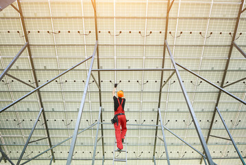 Wall Mural - Installing and wiring of solar photo voltaic panels. Back view of worker in orange uniform connecting solar panels at the station. Ecology power conservation concept.