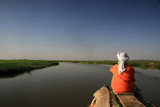 Fototapeta Mosty linowy / wiszący - mężczyzna siedzący tyłem na końcu czółna patrzący w dal płynący spokojną rzeką niger w mali