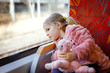 © Irina Schmidt - Cute little toddler girl sitting in train and looking out of window while moving. Adorable happy healthy baby child holding plush toy in hands. Smiling child going on family vacations by railroad
