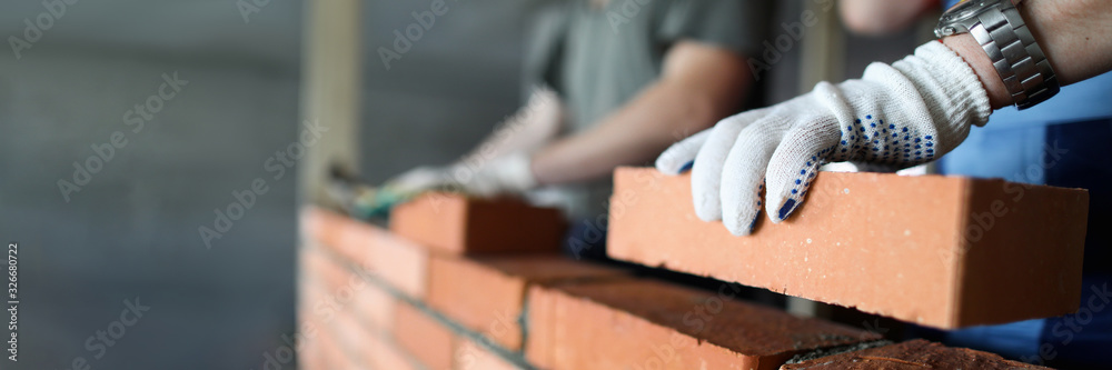 Two workers making red brick wall at construction site - obrazy, fototapety, plakaty 