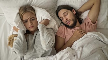 Sticker - A displeased disappointed young woman is covering her ears with a pillow while her boyfriend is snoring in the bed at the bedroom