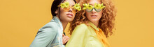 Panoramic Shot Of Attractive Multicultural Women In Sunglasses With Flowers Isolated On Yellow