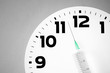 White clock dial and injection syringe indicating time against grey background. Vaccination time. Conceptual depiction of seasonal vaccination.	