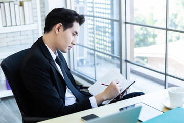 Happy mood a cheerful of asian young businessman have ideas make a note the successful business plan in a notebook and computer on wooden table background in office.