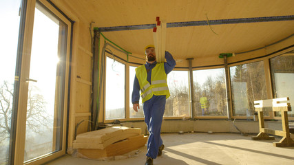 Wall Mural - LOW ANGLE: Worker arrives to work carrying heavy wooden beams on his shoulder