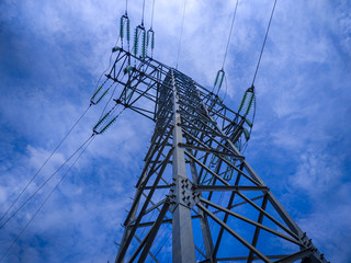 Top of electric transmission tower or power tower or electricity pylon and line of electric wires against a blue cloudy sky. Steel lattice tower, to support an overhead power line.