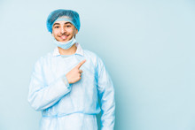 Young Arabian Surgeon Man Isolated Against On A Blue Background Smiling And Pointing Aside, Showing Something At Blank Space.