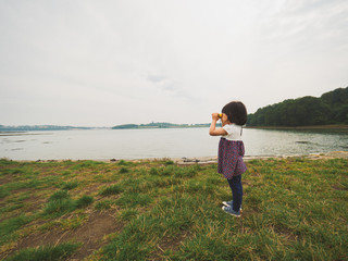 Wall Mural - toddler girl playing with telescope in countryside park,Northern Ireland