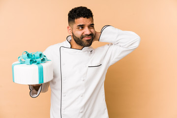 Young latin baker man holding a cake isolated touching back of head, thinking and making a choice.