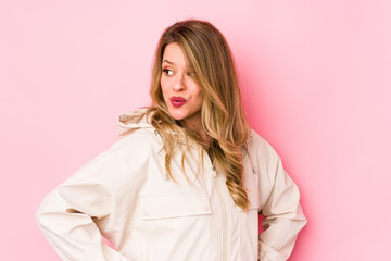 Young caucasian woman isolated on pink background looks aside smiling, cheerful and pleasant.