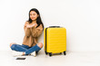 © Asier - Young chinese traveler woman sittting on the floor with a suitcase isolated holding something with palms, offering to camera.