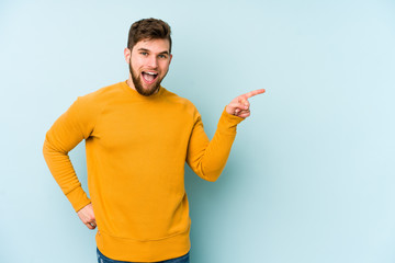 Wall Mural - Young caucasian man isolated on blue background smiling cheerfully pointing with forefinger away.