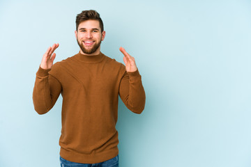 Wall Mural - Young caucasian man isolated on blue background holding something little with forefingers, smiling and confident.