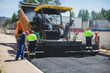 © tsuguliev - Asphalt paver machine and steam road roller during road construction and repairing works, process of asphalting and paving, workers working on the new road construction site, placing a layer, drone