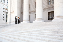 Two Well Dressed Professionals In Discussion On The Exterior Steps Of A Courthouse. Could Be Lawyers, Business People Etc.