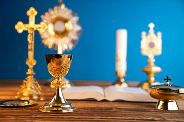 Wall Mural - Catholic religion concept. Catholic symbols composition. The Cross, monstrance,  Holy Bible and golden chalice on the altar. Blue background.