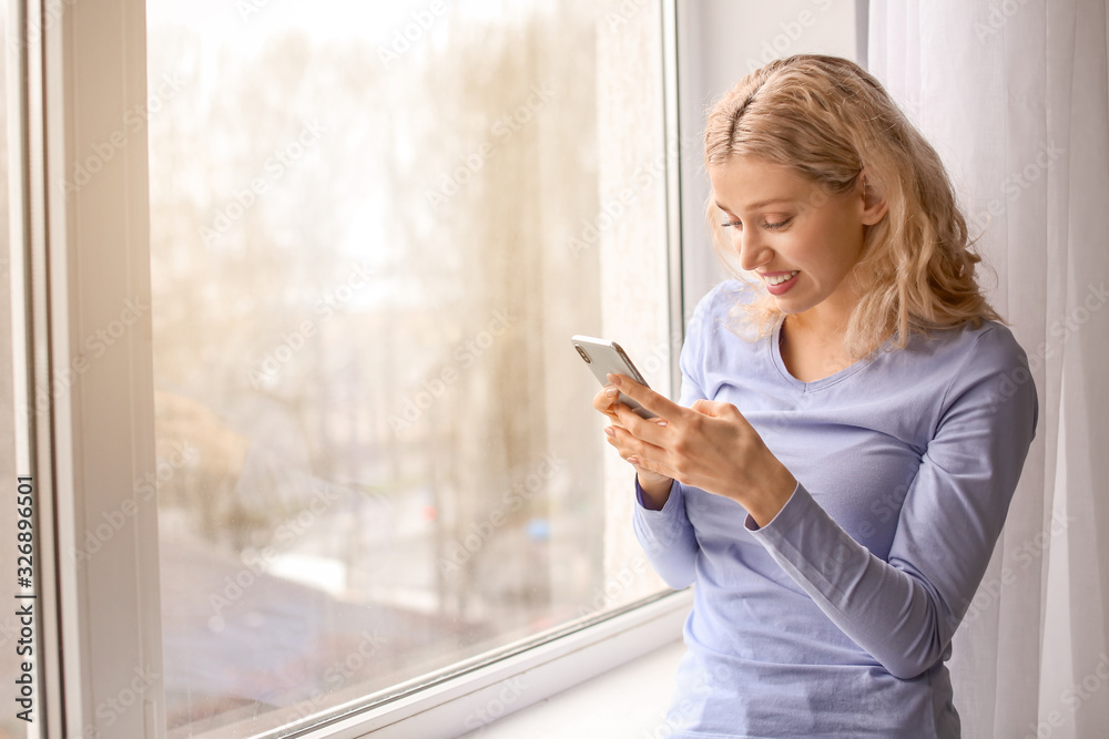 Young woman with mobile phone near window