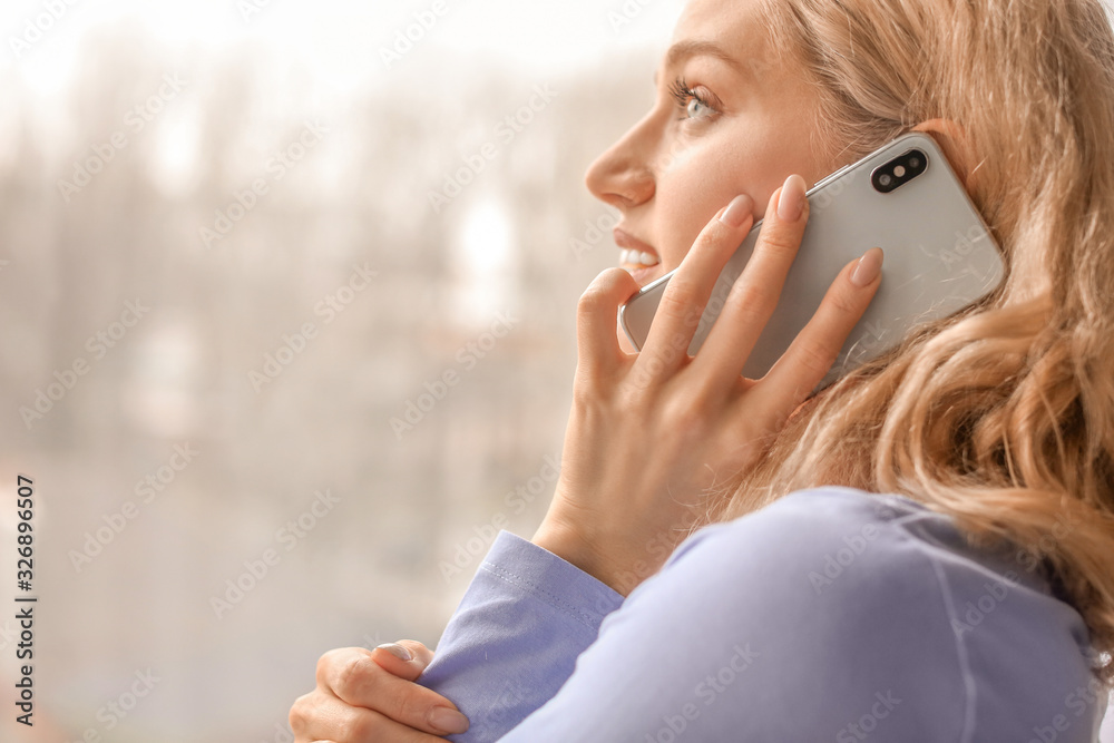 Young woman talking by mobile phone at home