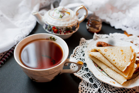 A beautiful version of Breakfast with a white porcelain Cup and a painted teapot in the background, ready-made pancakes on a saucer. Table setting for the Russian holiday Maslenitsa