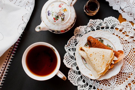 A beautiful version of Breakfast with a white porcelain Cup and a painted teapot in the background, ready-made pancakes on a saucer. Table setting for the Russian holiday Maslenitsa. Flatlay, top view