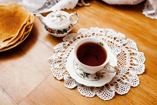 A beautiful version of Breakfast with a white porcelain Cup on a knitted white napkin and a painted teapot in the background, ready-made pancakes on a saucer. Table setting for the Russian Maslenitsa.