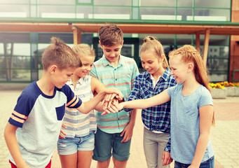 Wall Mural - primary education, friendship, childhood and people concept - group of happy elementary school students with hands on top outdoors