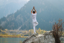 A Zen Man In White Practices Yoga In Nature. Pose Vrikshasana Or Tree Pose