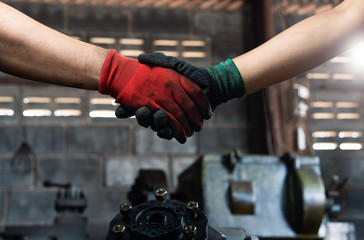 Male and female industrial workers shaking hands in factory workshop wearing protective workwear - Business and commercial teamwork within the workplace - Working together, goals and success concept