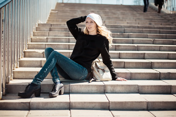 Wall Mural - Fashion photo of a young beautiful woman in jeans, a black sweatshirt, a white knitted hat with a backpack