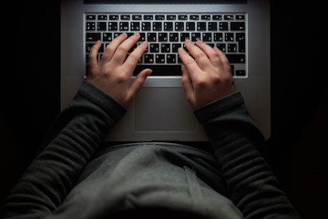 Overhead hacker in the hood working with laptop and mobile phone typing text in the darkroom. Russian hacker hacking the server in the dark. A hacker girl sitting in the dark with her laptop