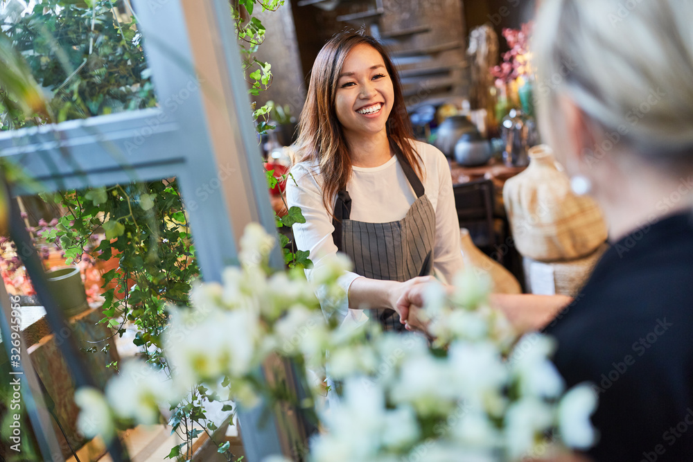 Florist welcomes customer with handshake in flower shop - obrazy, fototapety, plakaty 