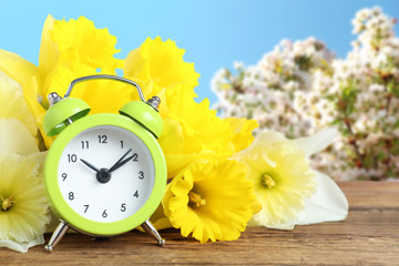 Poster - Alarm clock and flowers on wooden table against blurred background. Spring time